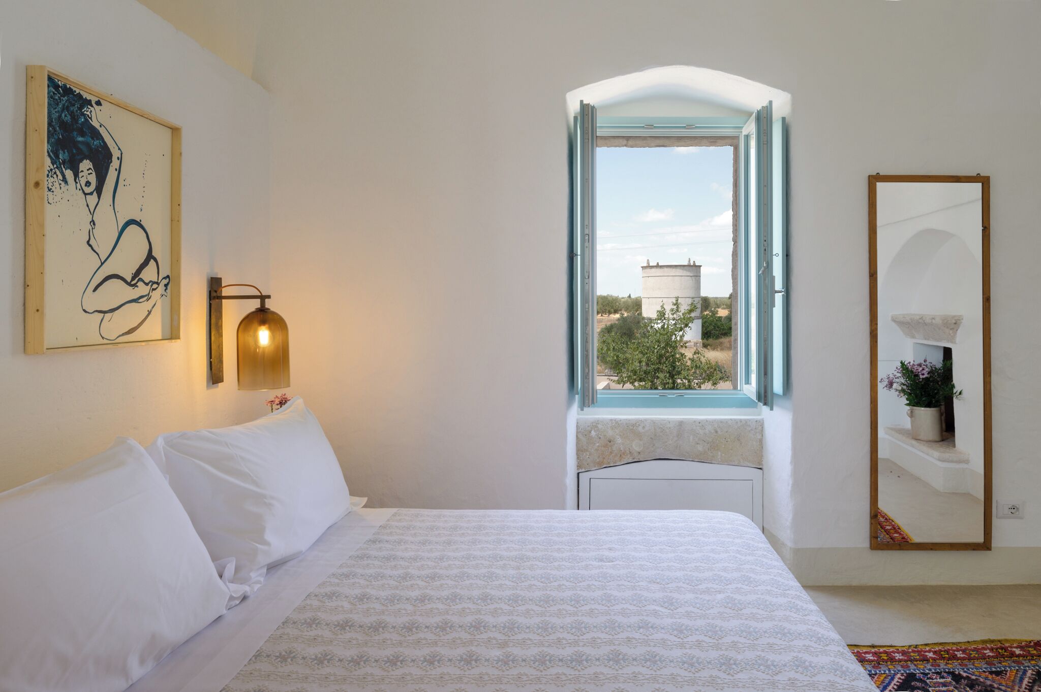 Un dormitorio con cama, ventana con vista despejada, lámpara de pared e imagen enmarco.