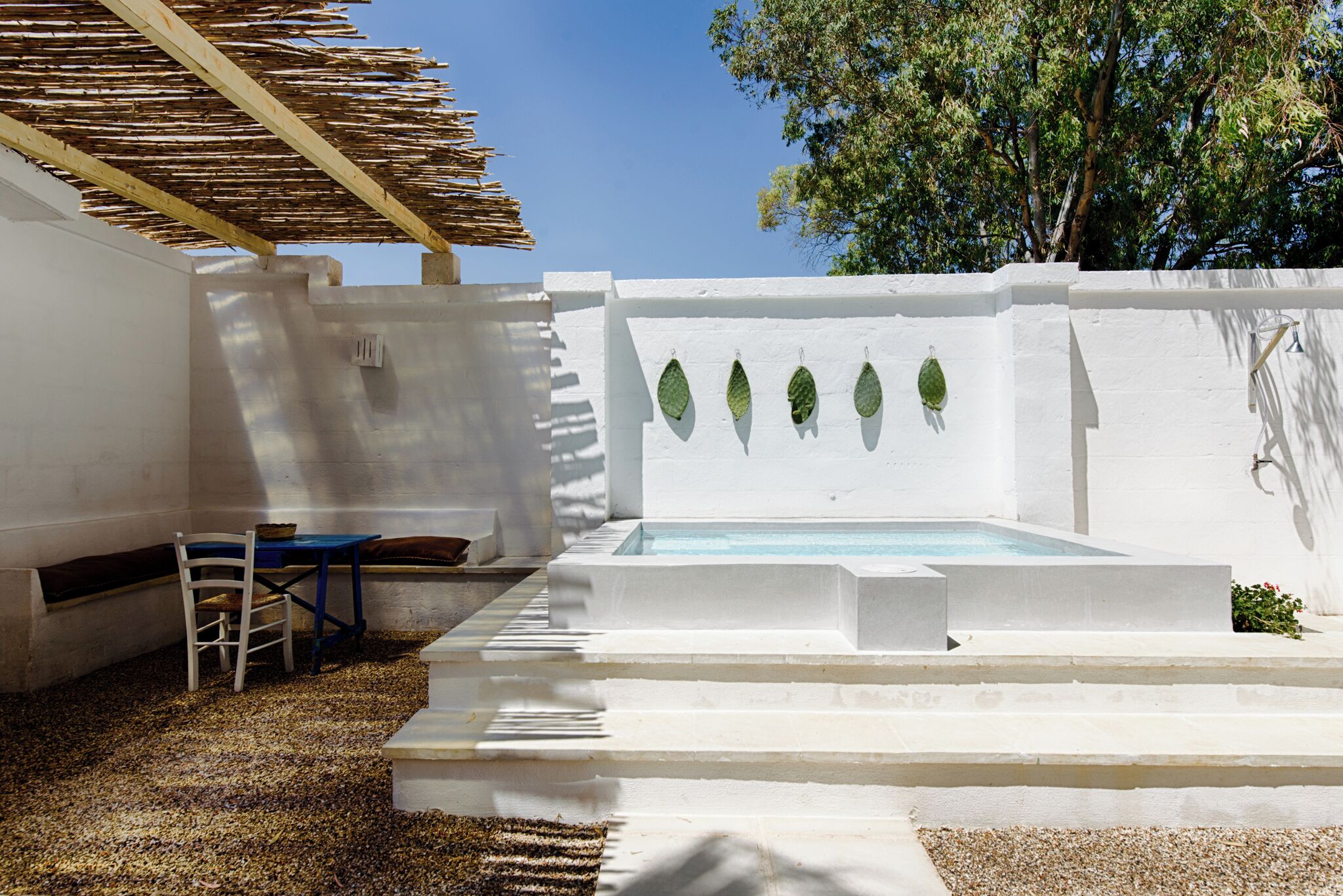 Ein Außenbereich mit weißen Wänden, einem Pool, einer Holz-Pergola und einer Sitzgruppe.