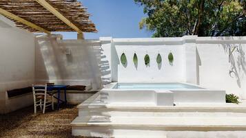 Ein Außenbereich mit weißen Wänden, einem Pool, einer Holz-Pergola und einer Sitzgruppe.