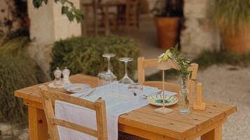 Un tavolo da esterno in legno apparecchiato con una tovaglia bianca, bicchieri da vino e un vaso con fiori.