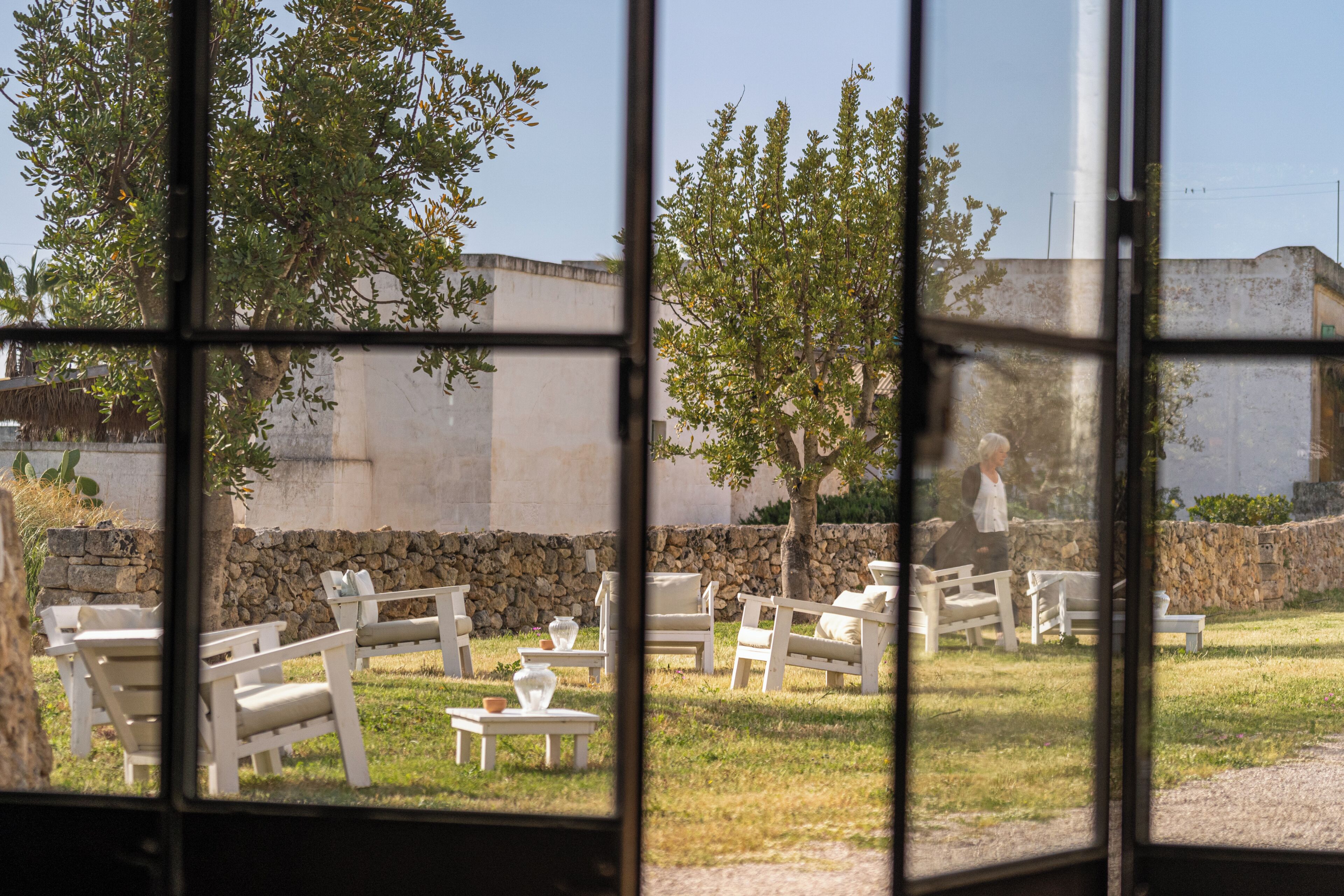 Vista desde una ventana que muestra una terraza al aire libre con muros de piedra y árboles.