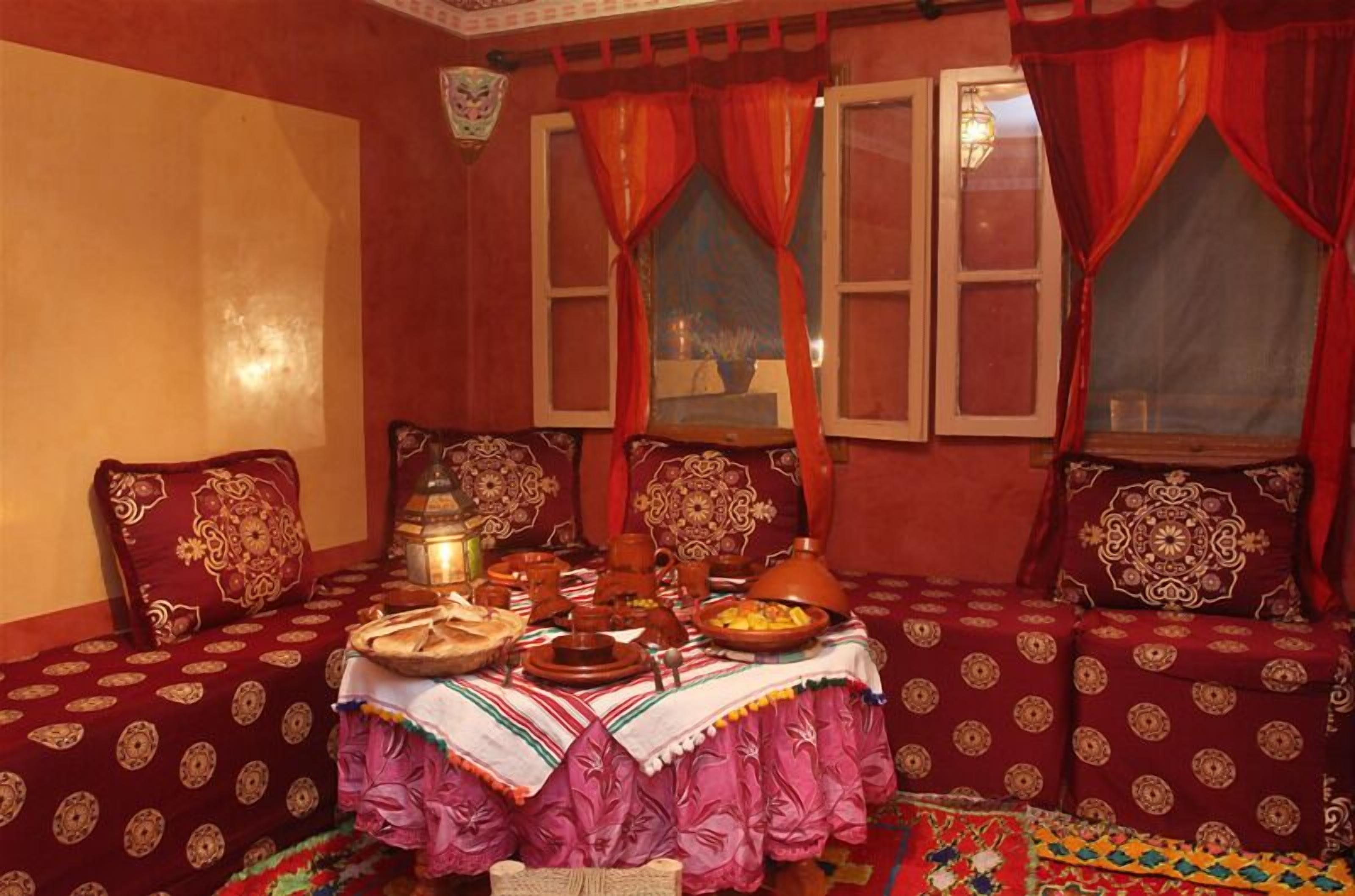 Een traditionele Marokkaanse kamer met een gestreept bankstel, een tafel met een theeset en decoratieve kussens.