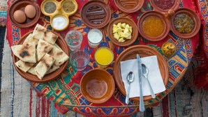 Una comida tradicional dispuesta con varios platos y utensilios sobre un mantel tejido y colorido.