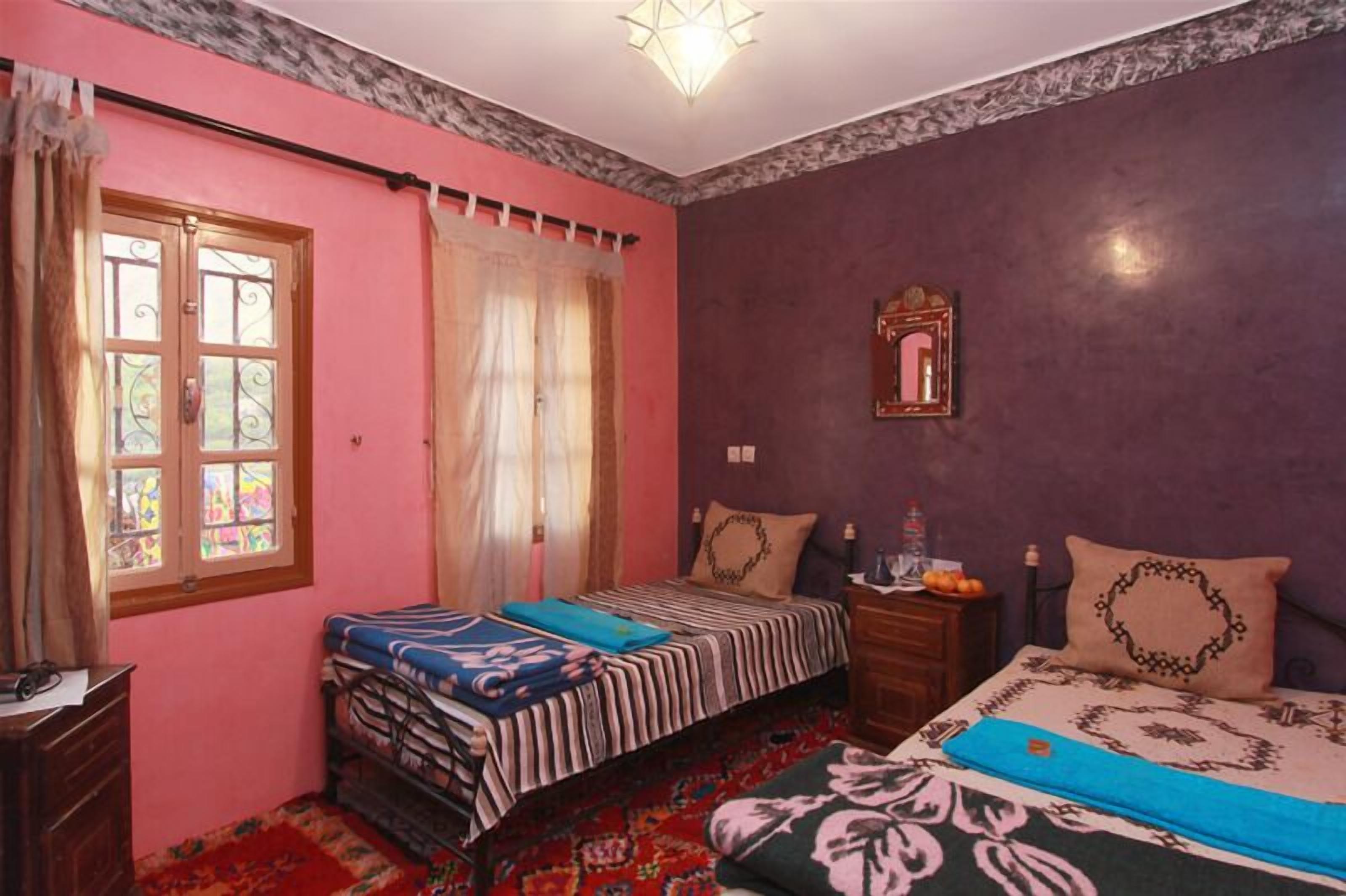 A bedroom with two beds, a dresser, a nightstand, a mirror, and a window with curtains.