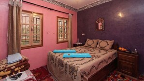 Un dormitorio con cama, dos ventanas, una mesita de noche y un espejo en la pared.