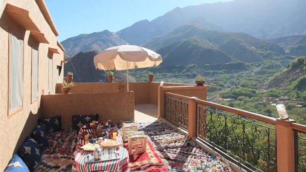 Un balcón con vista a montañas, una mesa con mantel a rayas y un paraguas color beige.