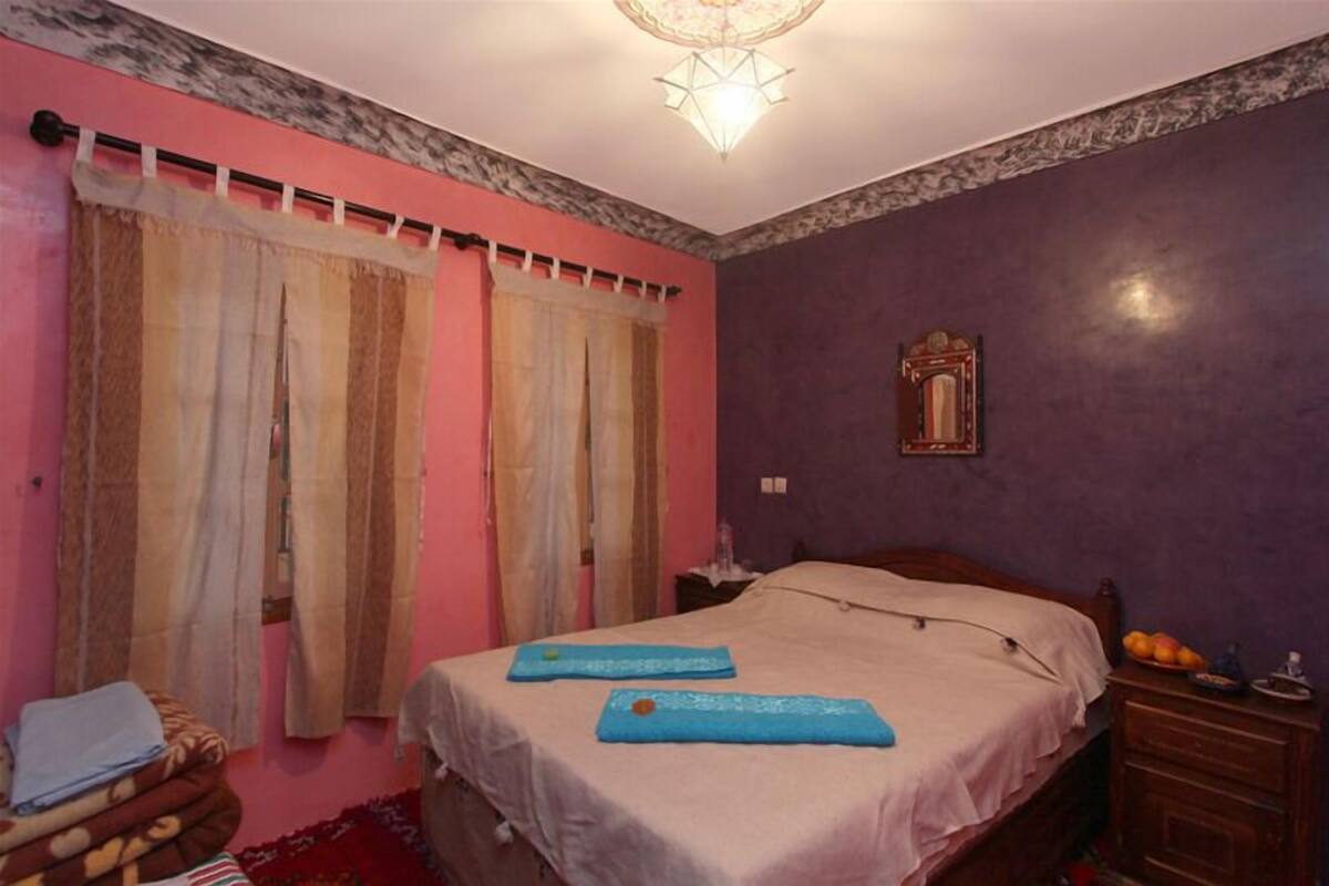 A bedroom with a bed, curtains, a nightstand, and a mirror.