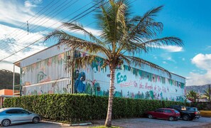 A building with a mural, a palm tree, and cars parked in front. - Eco Encanto Pousada (Ubatuba)