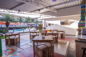 An outdoor patio area with wooden tables and benches, a pool in the background, and a colorful wall decoration. - Eco Encanto Pousada (Ubatuba)