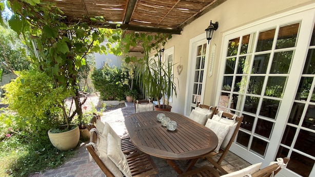 A patio with a wooden table and chairs, surrounded by potted plants and a brick floor. - Jonquil Cottage (Franschhoek)