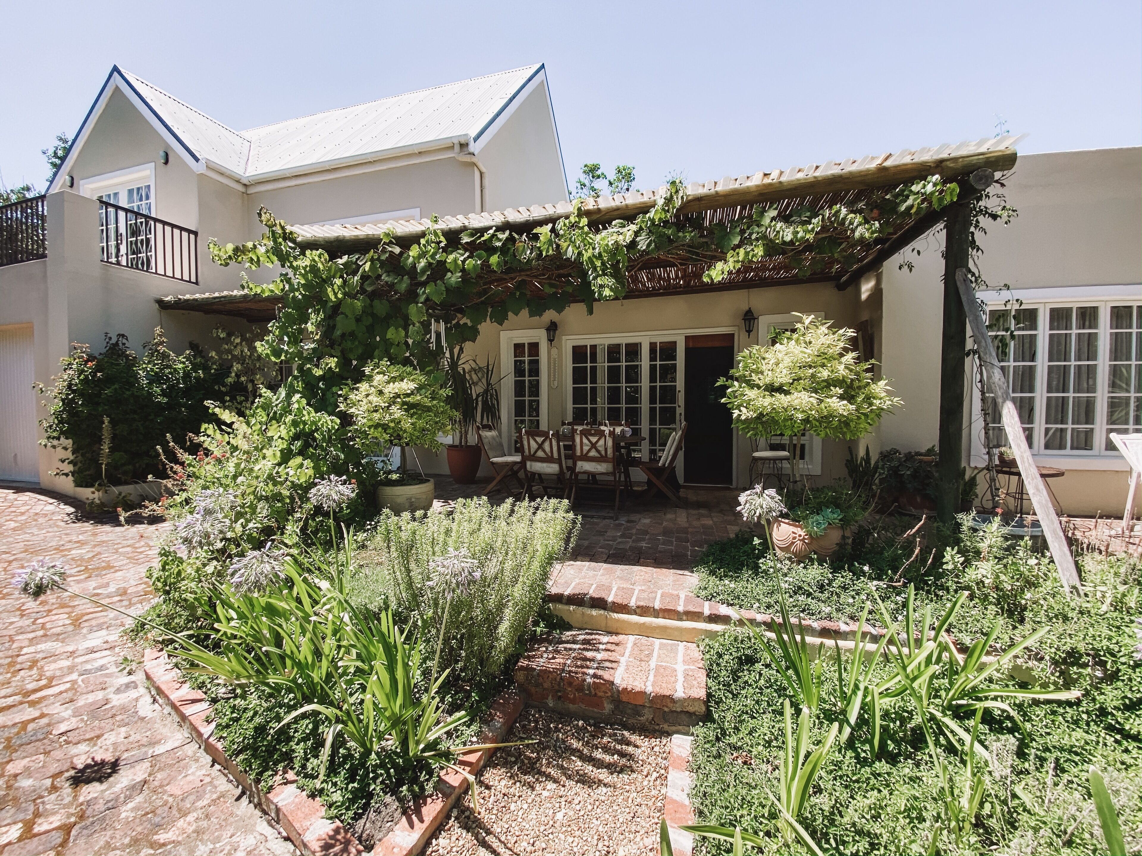 A house with a covered patio, potted plants, and a brick pathway leading to the entrance.