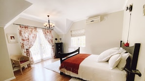 A bedroom with a bed, a chair, a window, and a chandelier. - Jonquil Cottage (Franschhoek)