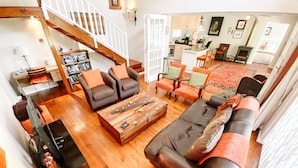 A spacious living room with a wooden floor, a large sofa, two armchairs, and a coffee table. A staircase with wooden railings leads to an upper level. - Jonquil Cottage (Franschhoek)