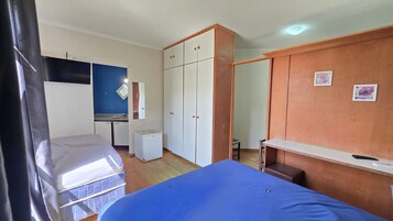 Una habitación con cama, escritorio, armario y un refrigerador pequeño.