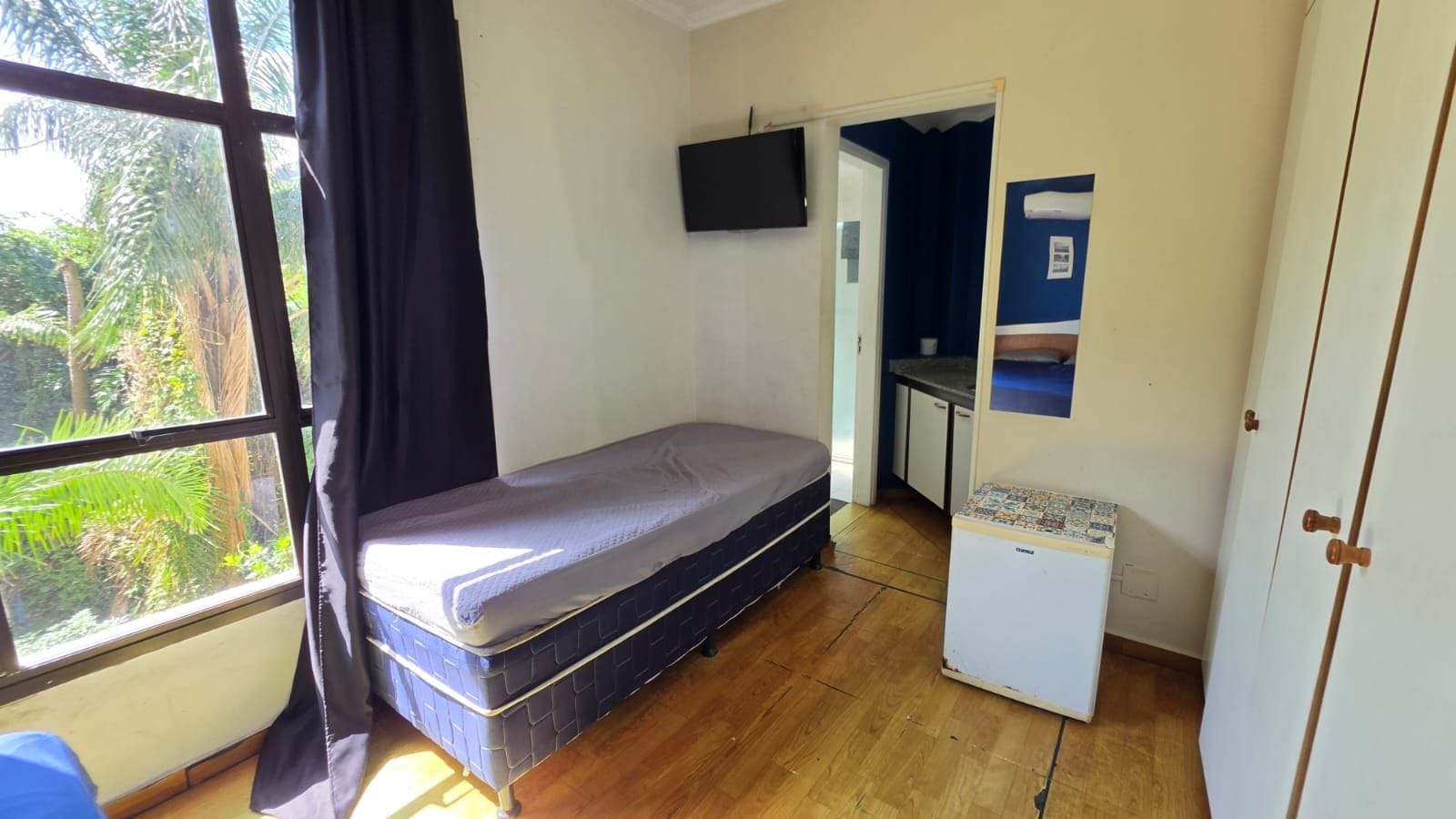 Una stanza con un letto, un angolo cottura e una TV appesa al muro.