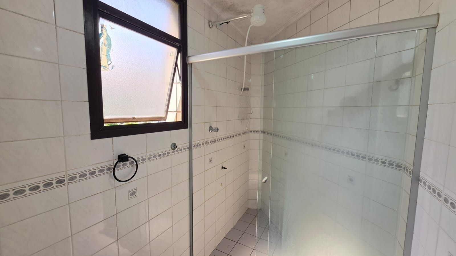 Ein Badezimmer mit weißen Fliesen, einer Glasdusche, einem Fenster mit Aussicht und einem Handtuchhalter.