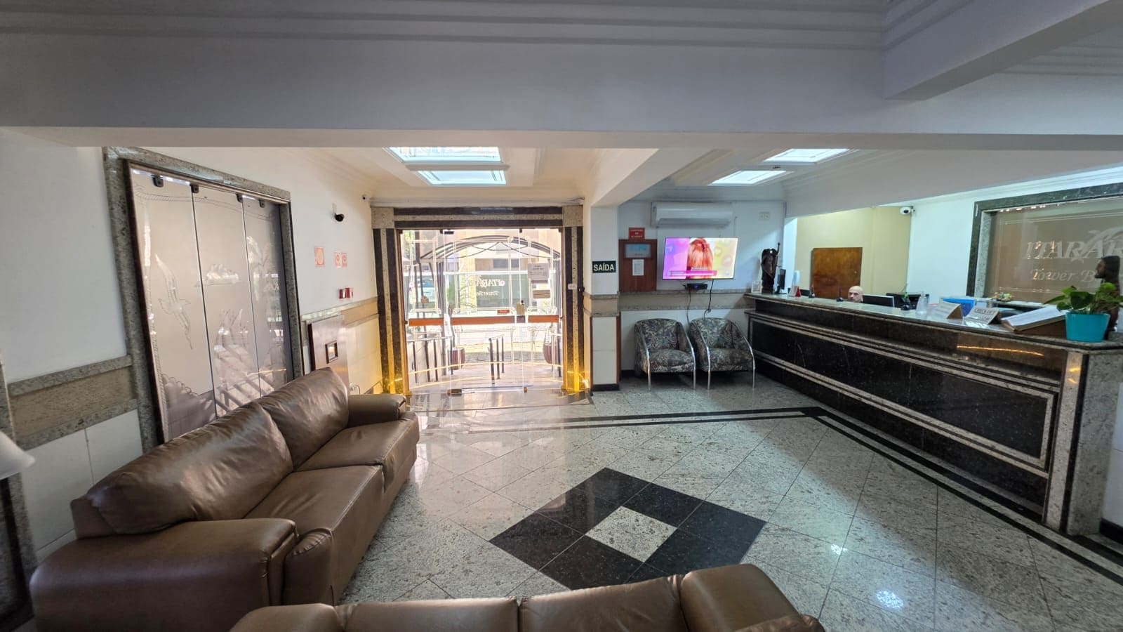 Zona de recepción con sofá, sillas, mostrador de recepción y puerta de vidrio que da al exterior.