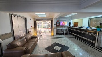 Zona de recepción con sofá, sillas, mostrador de recepción y puerta de vidrio que da al exterior.