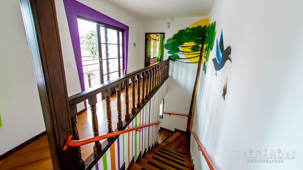 A staircase with a wooden handrail and orange handrails, leading to a room with a purple door and a window with a view of the outside. - Curitiba Casa Hostel (Curitiba)