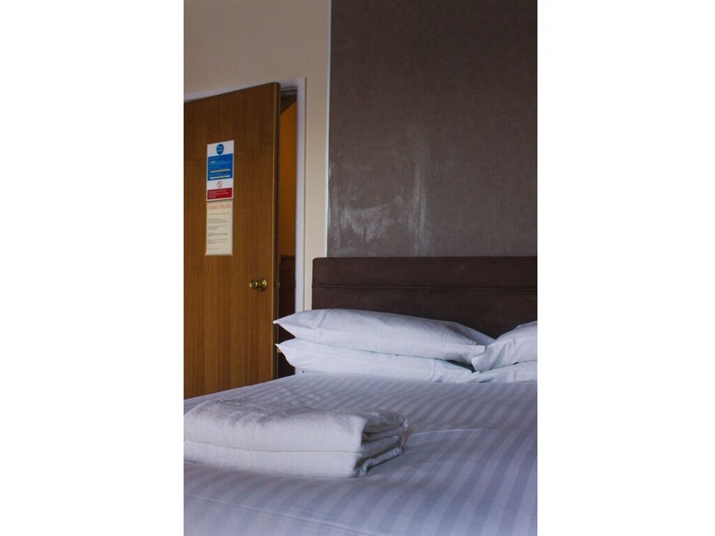 Habitación de hotel con puerta de madera, cama con ropa blanca y pared lisa.