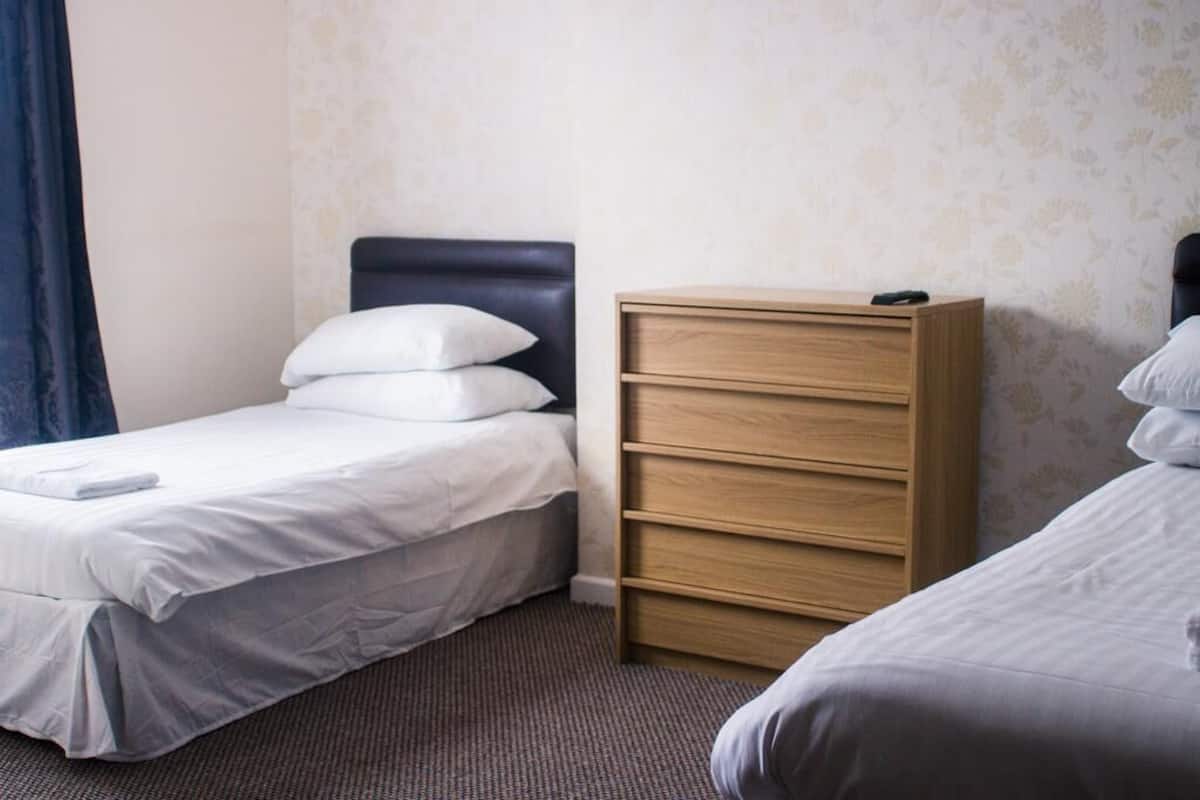 A hotel room with two single beds, a wooden dresser, and a patterned wallpaper.