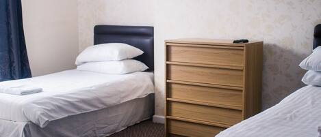 A hotel room with two single beds, a wooden dresser, and a patterned wallpaper.