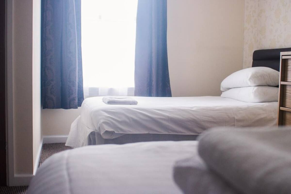 A hotel room with a bed, a nightstand, and a window with curtains.