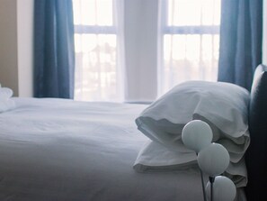 Un lit avec une literie blanche et un oreiller agrémenté d’un élément décoratif blanc.