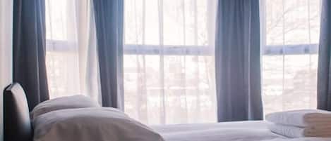 A hotel room with a bed, pillows, and a window with curtains.