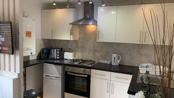Una cocina moderna con armarios blancos, estufa a gas, horno empotrado y cafetera.
