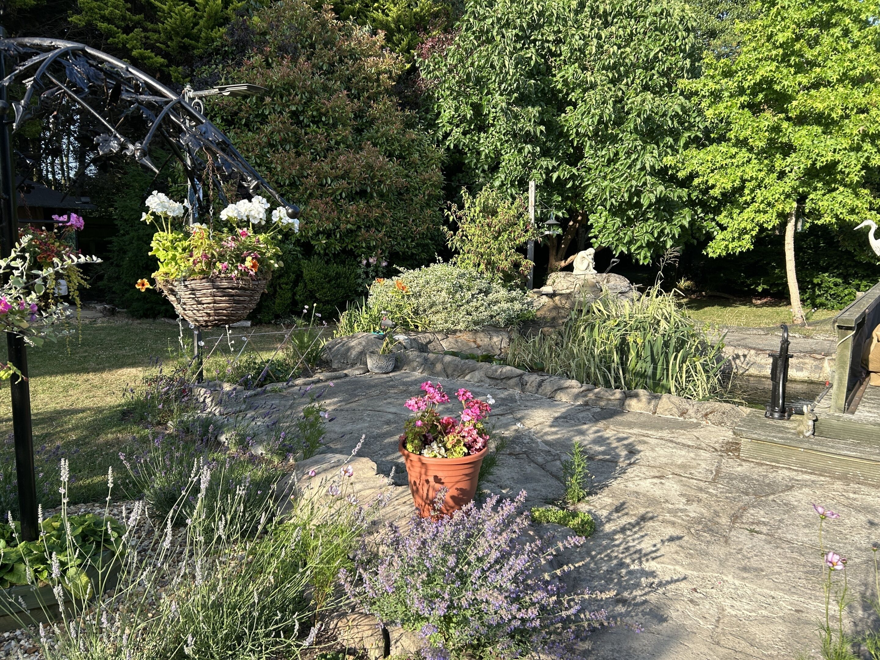 Un jardin agrémenté d’une arche en métal, d’un sentier en pierre et de diverses plantes en pot.