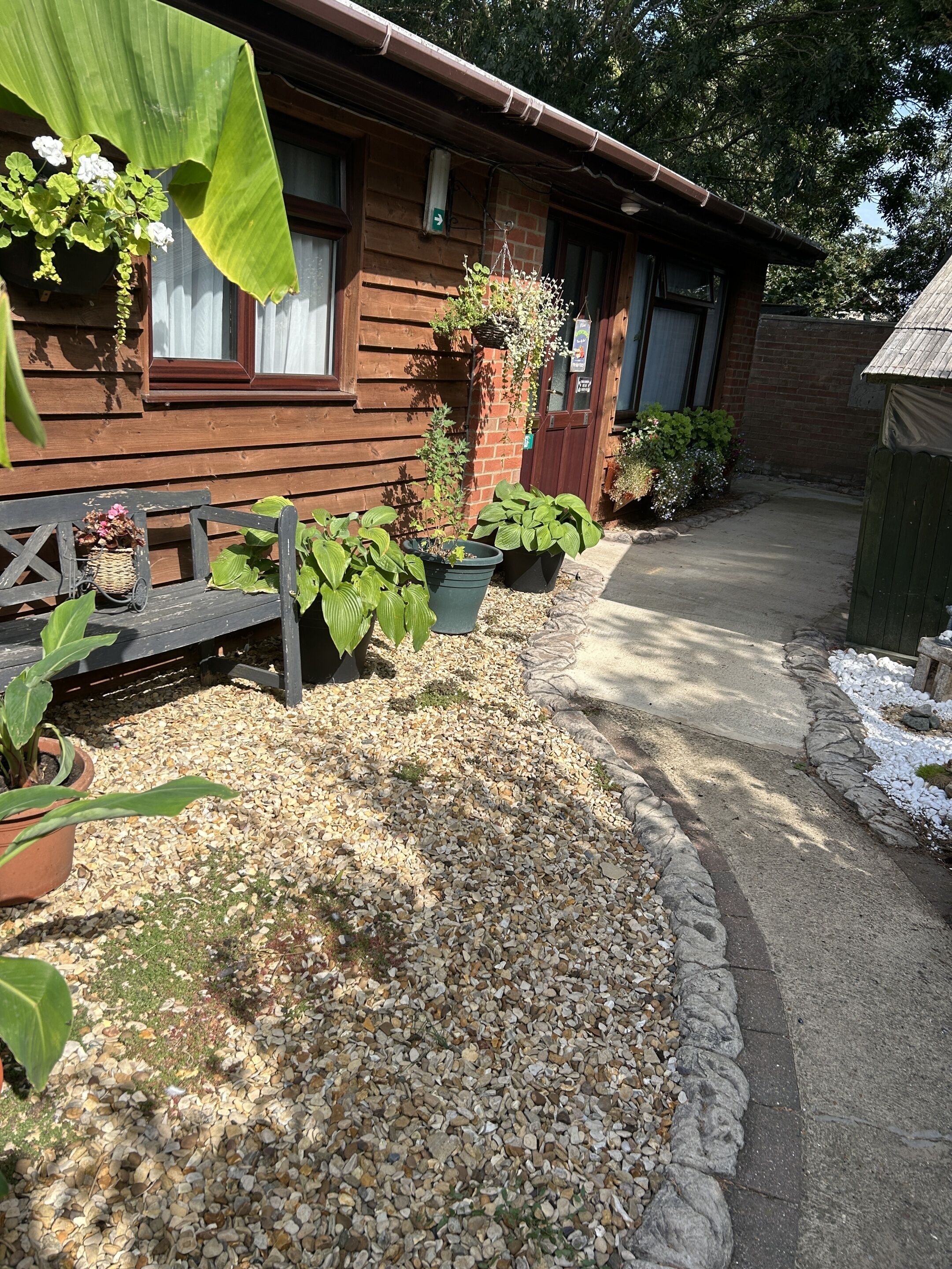 A wooden house with a gravel pathway, potted plants, and a bench.