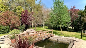A garden with a wooden bridge over a pond, surrounded by various trees and plants. - Woodpaddock B&B (March)