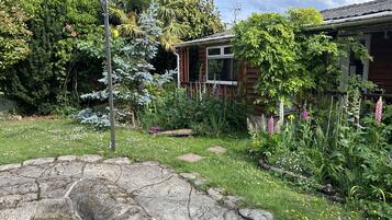 A garden with a stone fountain, lush greenery, and a wooden house.
