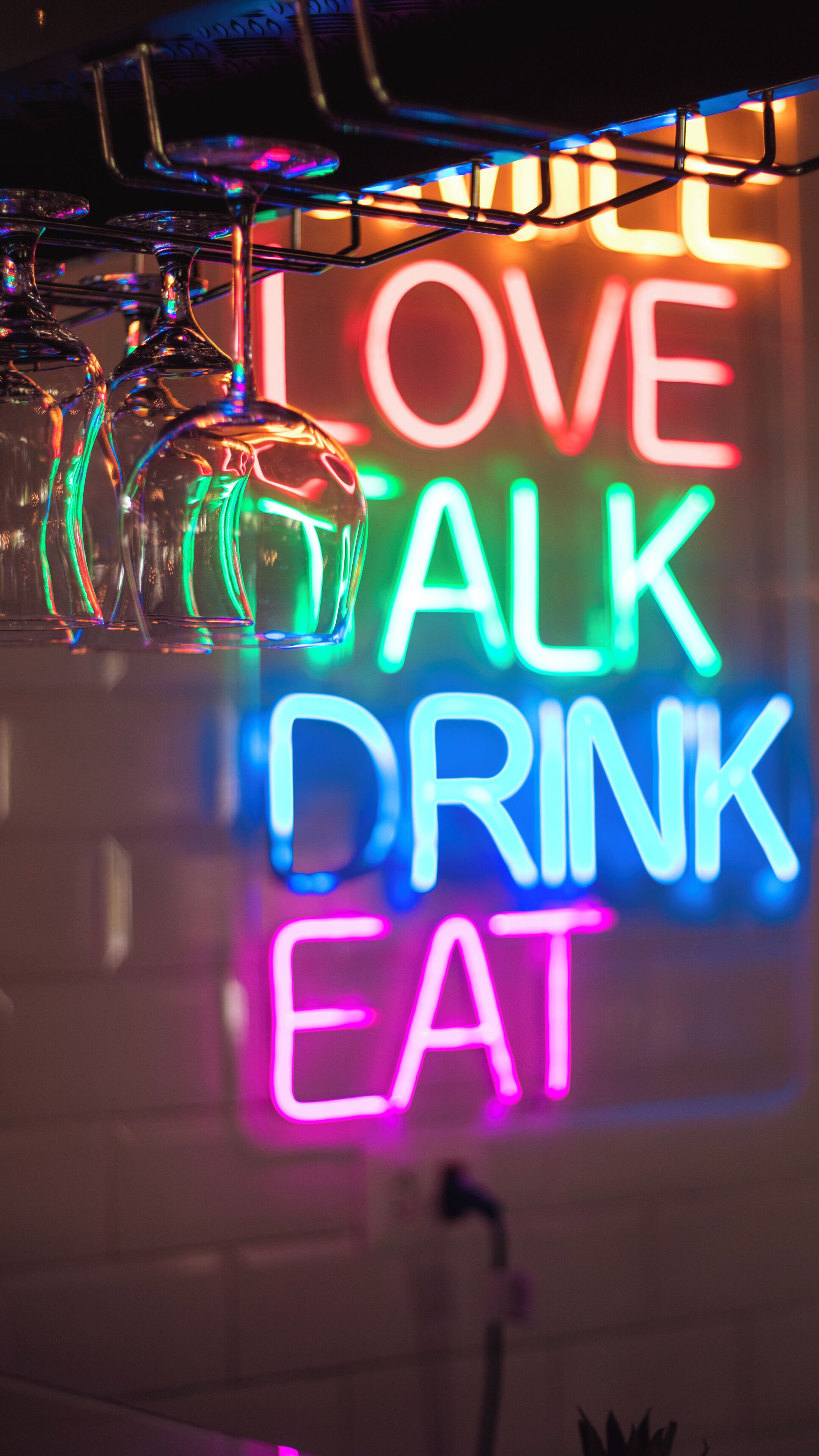 A neon sign with the words 'LOVE TALK DRINK EAT' in a room with hanging glassware.