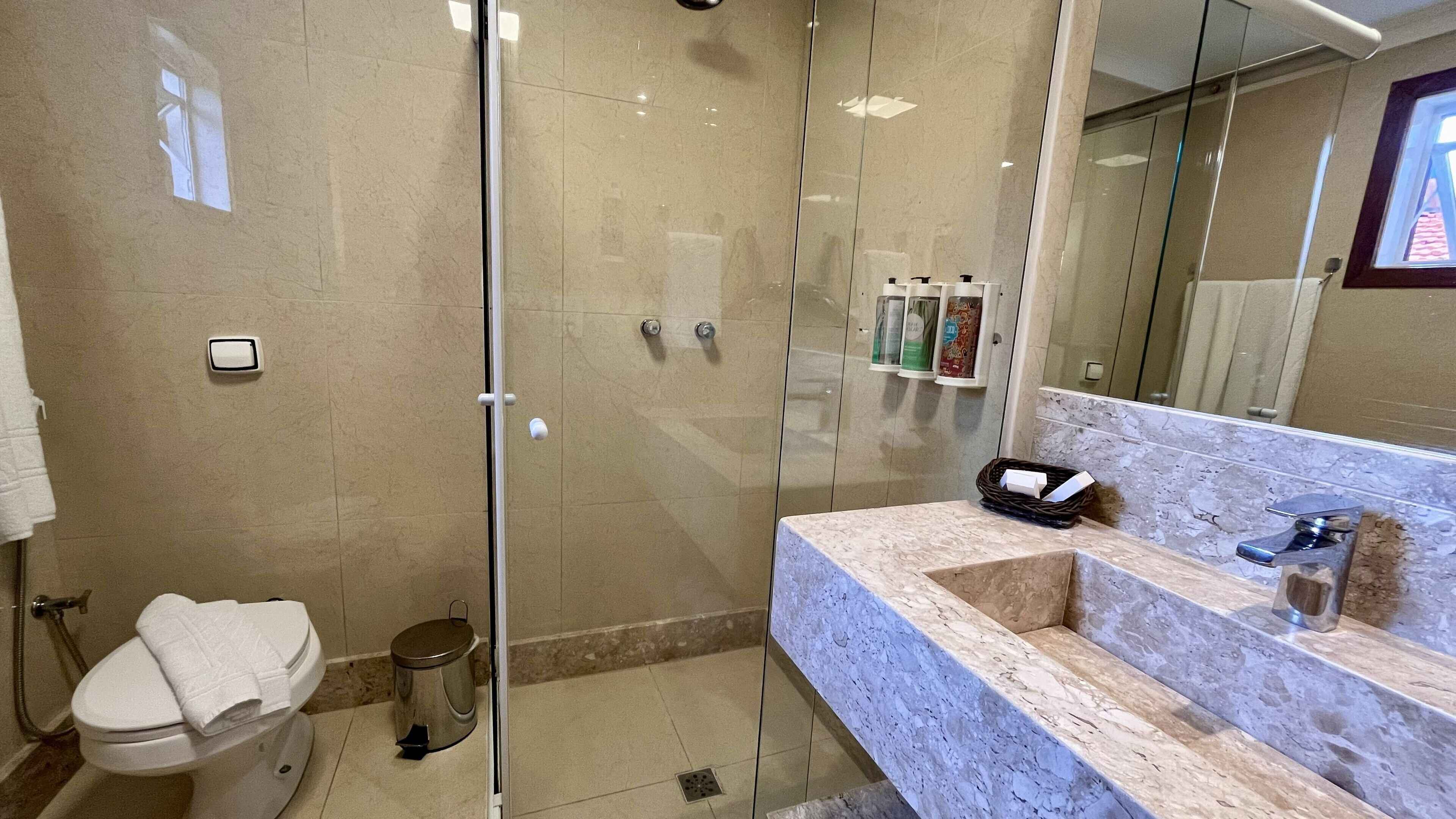 Un baño moderno con cabina de ducha de vidrio, inodoro y lavamanos de mármol con espejo.