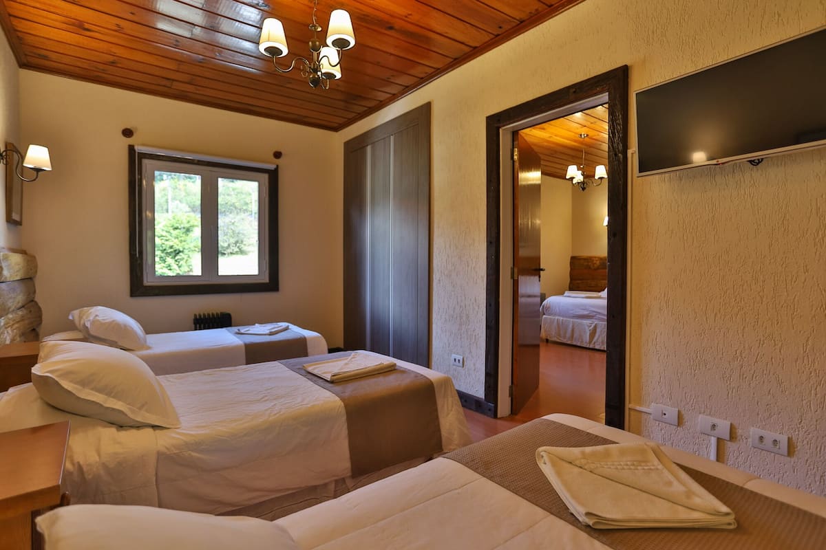 A room with two beds, a window, a mirror, and a wooden ceiling.