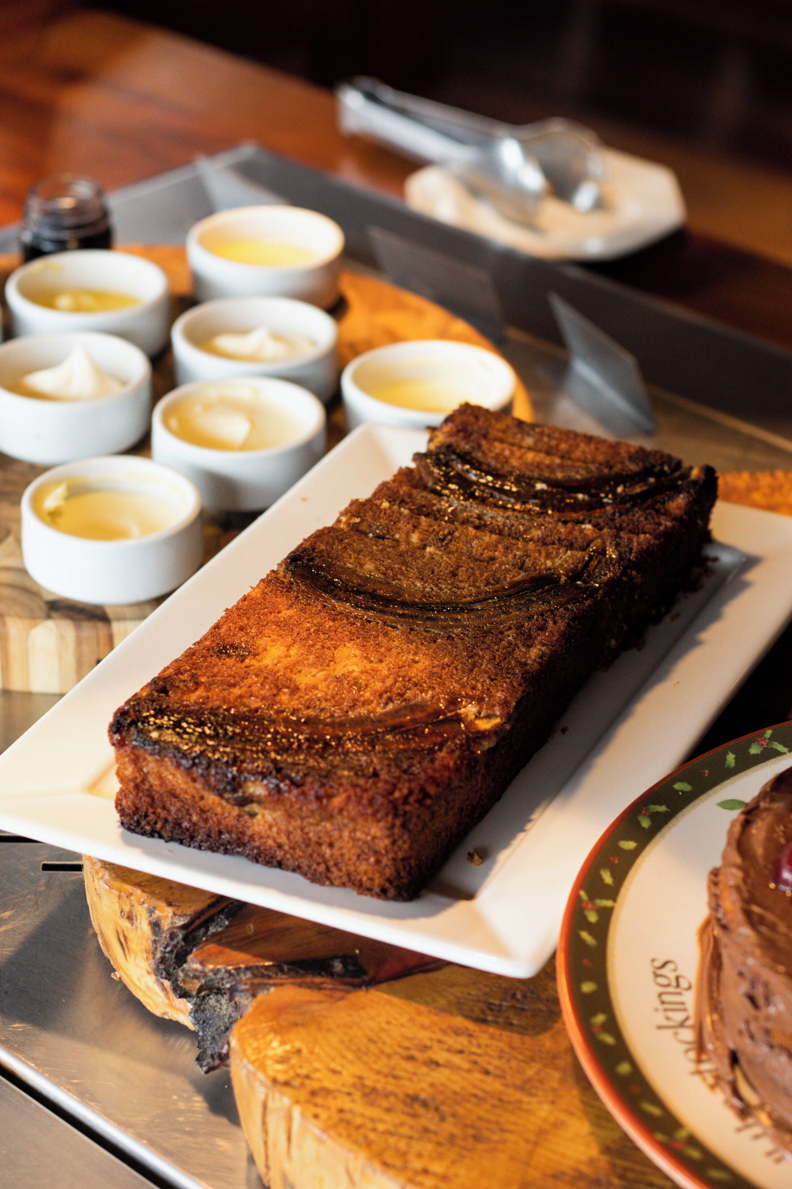 A tray with a rectangular baked dish, possibly a bread pudding, accompanied by small bowls of cream or butter.
