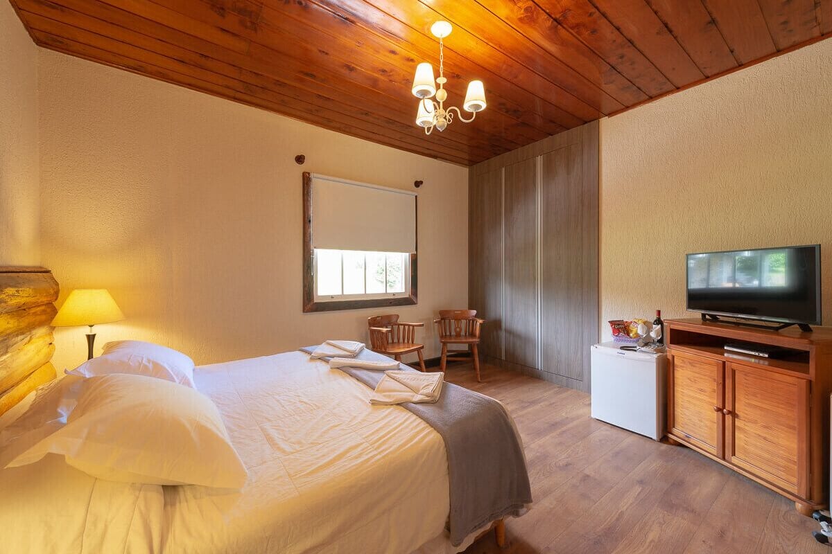 A hotel room with a wooden ceiling, a bed with white linens, a television on a wooden cabinet, and a small refrigerator.