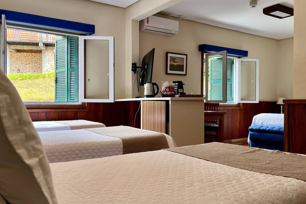 A hotel room with two beds, a desk with a computer, a coffee maker, and a window with shutters.