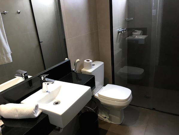 Casa de banho moderna com lavatório em bancada preta, sanita branca e cabine de duche em vidro.