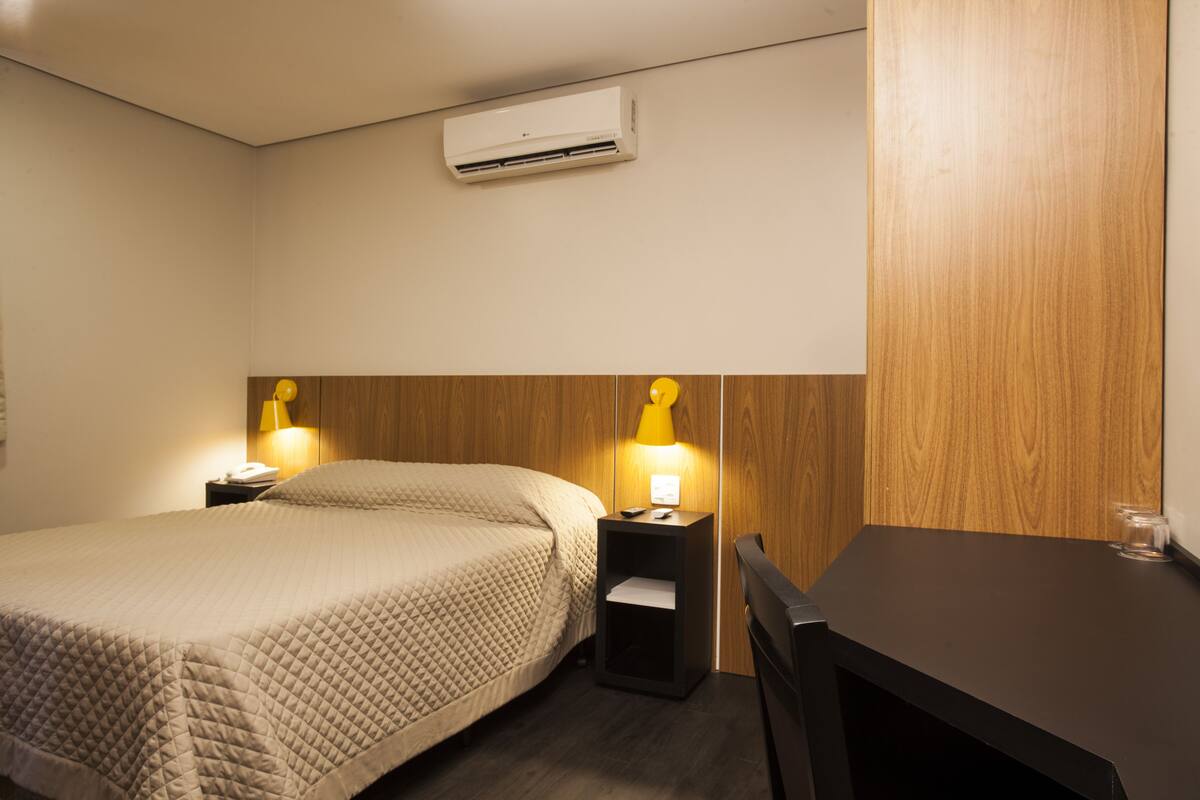 Ett hotellrum med en säng, sängbord, ett skrivbord och en luftkonditioneringsanläggning.