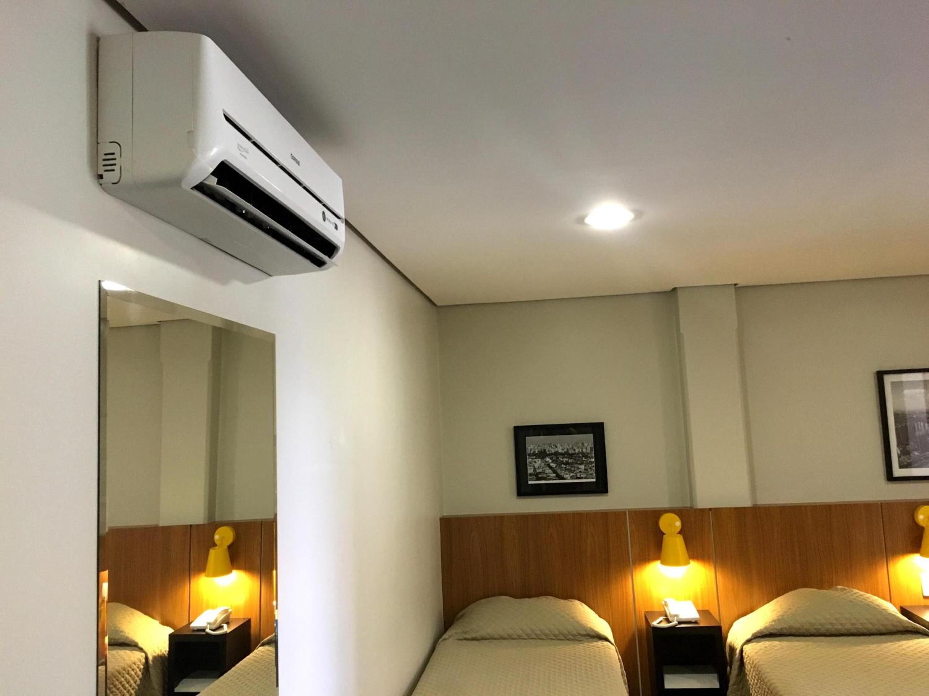 Une chambre d’hôtel comprenant un lit, deux tables de chevet avec des lampes, un climatiseur fixé au mur et un tableau encadré accroché au mur.