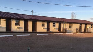 Un motel de dos pisos con techo rojo y paredes color beige. Se observan varias ventanas y puertas, además de un camino de entrada de grava.