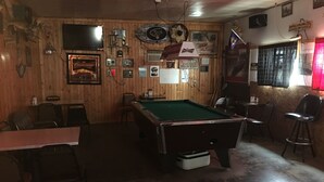 Una sala de billar con mesa de billar, sillas y diversos recuerdos en las paredes.
