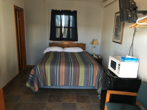 A hotel room with a bed, a nightstand, a lamp, a microwave, and a chair.