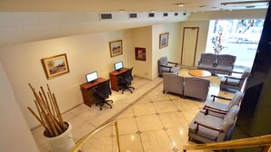 Un vestíbulo de hotel con una recepción, computadoras, zona de estar y una escalera.