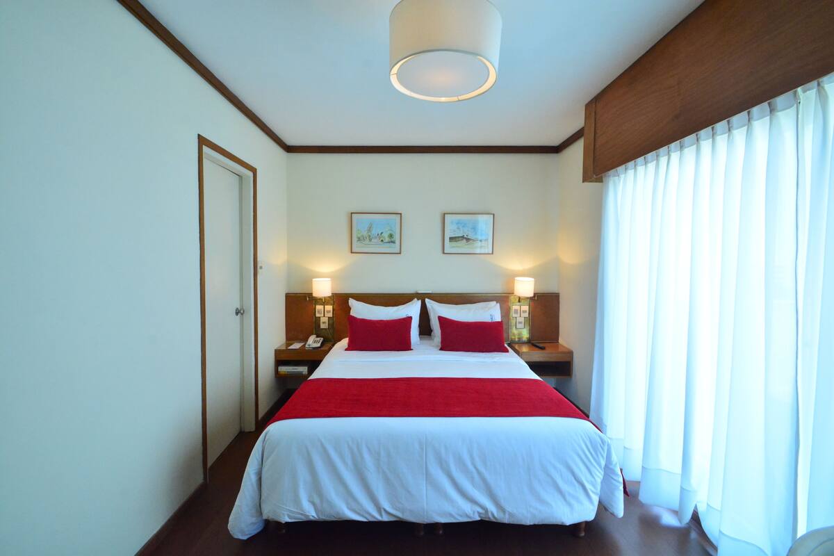 A hotel room with a large bed, two bedside tables with lamps, a door, and two framed pictures on the wall.