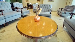 Un vestíbulo con cuatro sillones azul claro dispuestos alrededor de una mesa redonda de madera y un jarrón de cobre.