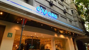 El exterior del Oxford Hotel, con una fachada moderna, amplios ventanales de vidrio y un llamativo letrero de neón.